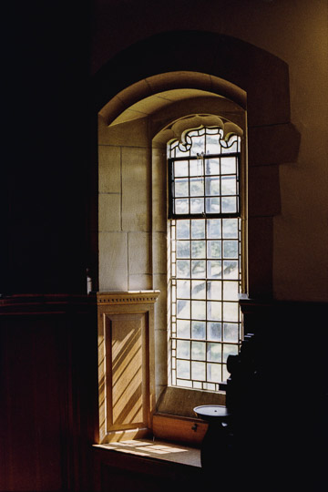 A photo of a sunlit window at the Carmarthen musuem chapel, casting light along the wooden wall.