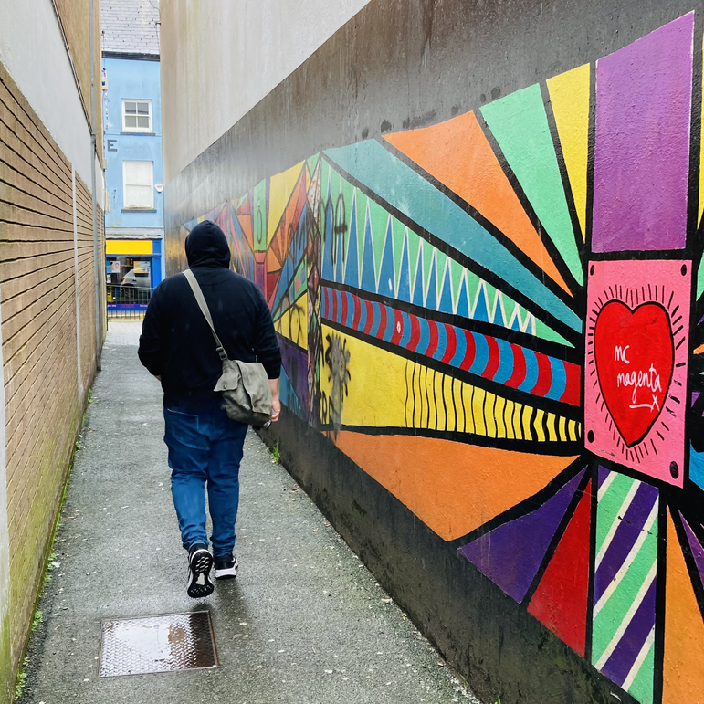 A picture of me walking down an alley with a bright coloured mural to the right of the image